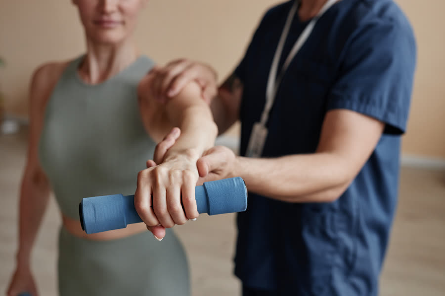 Physical therapist assisting a patient with a dumbbell strengthening exercise